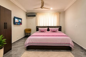 A bedroom with a bed, a ceiling fan, a TV on the wall, a chair, and a plant. - Cozy 1-bedroom apartment in adorable Spintex with AC (Spintex)