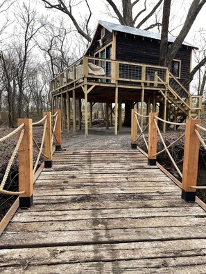 A wooden deck leading to a rustic cabin with a balcony, surrounded by trees.