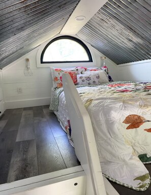 A small, attic-style bedroom with a sloped ceiling, a single bed with floral bedding, and a window providing natural light. - Fun & Magical Treehouse (Coweta)