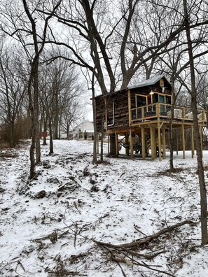 A wooden treehouse structure with multiple levels, surrounded by snow-covered ground and leafless trees. - Fun & Magical Treehouse (Coweta)