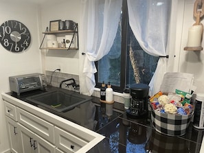 A kitchen with a black countertop, a toaster, a sink, a window with sheer curtains, and a bowl of snacks. - Fun & Magical Treehouse (Coweta)