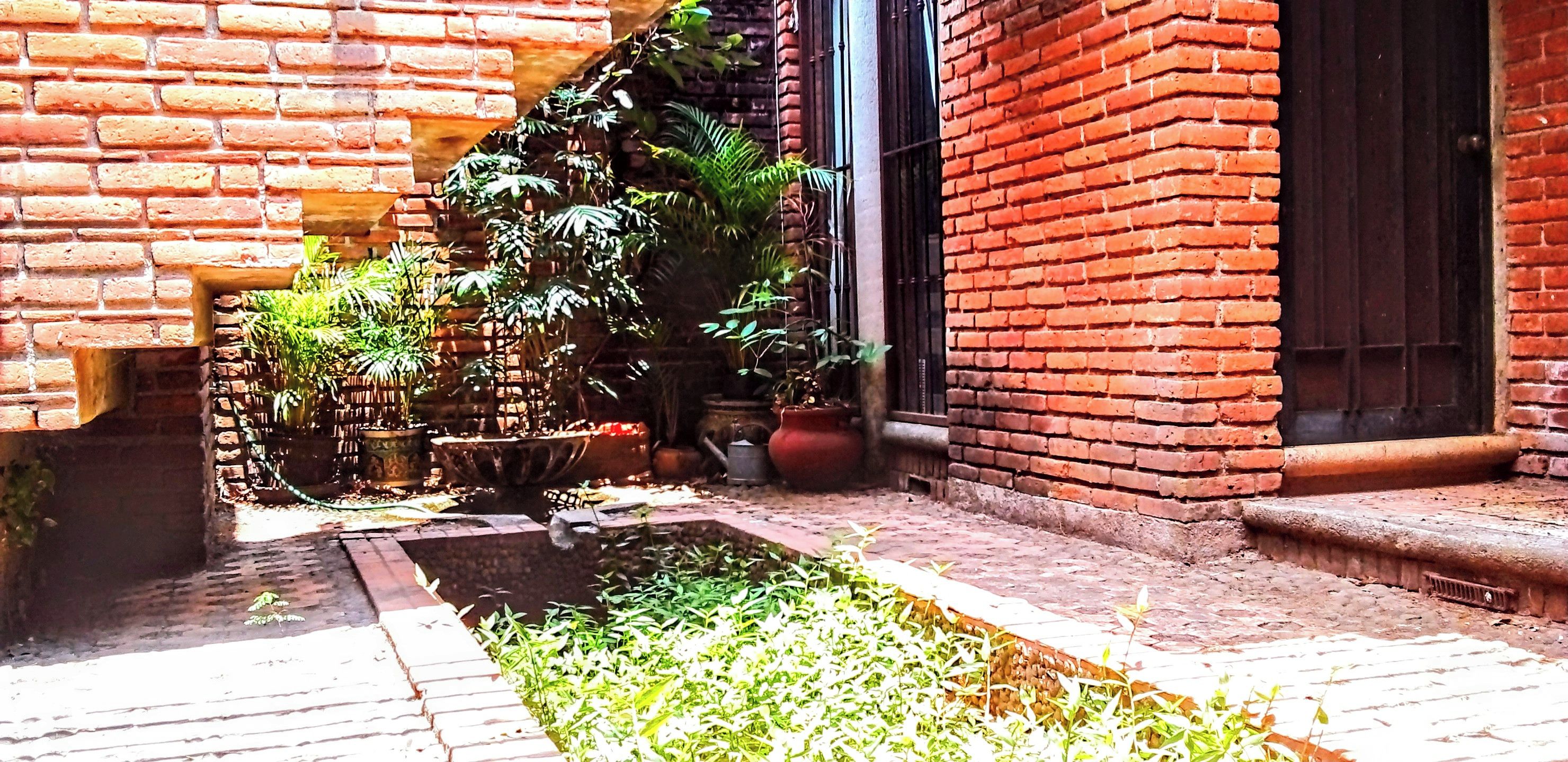 A courtyard with a brick wall, potted plants, and a small water feature.