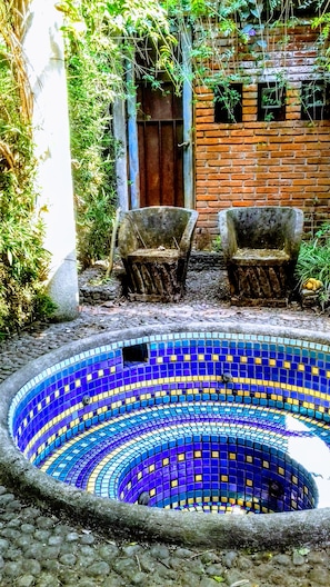 A circular mosaic pool with a brick wall and two chairs in the background.