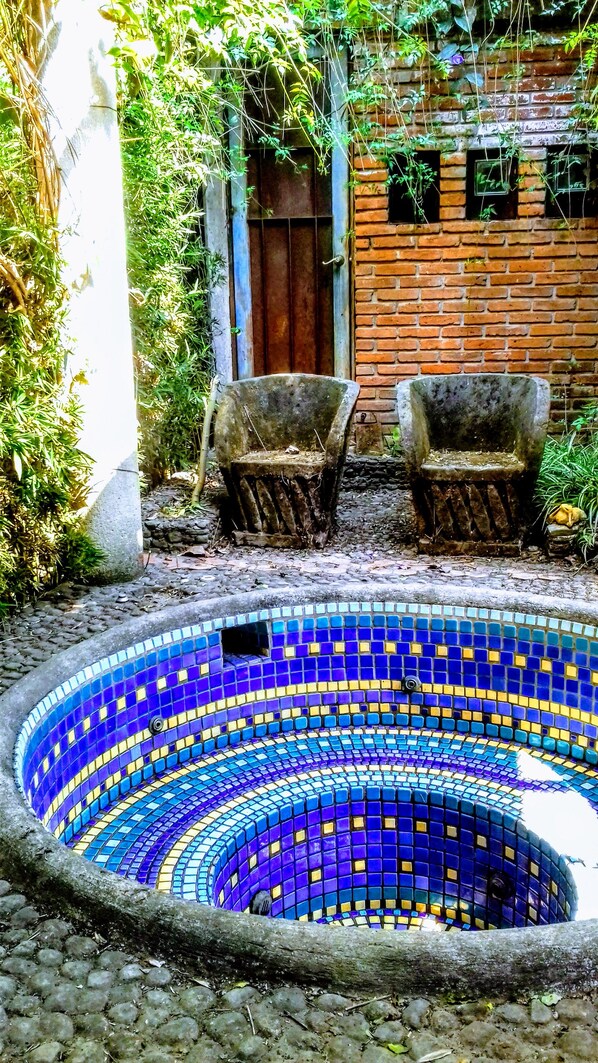 Une piscine circulaire ornée d’une mosaïque, avec un mur en briques et deux chaises en arrière-plan.