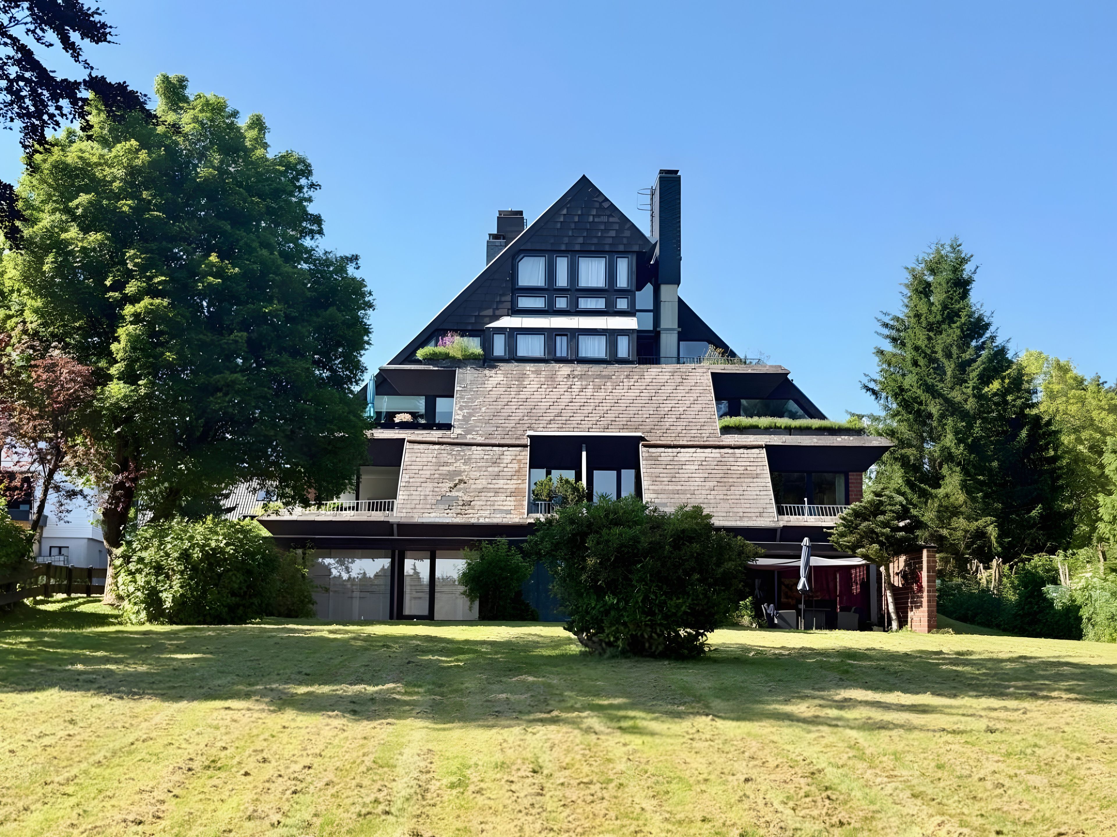 A modern two-story house with a sloped roof, large windows, and a well-maintained lawn.