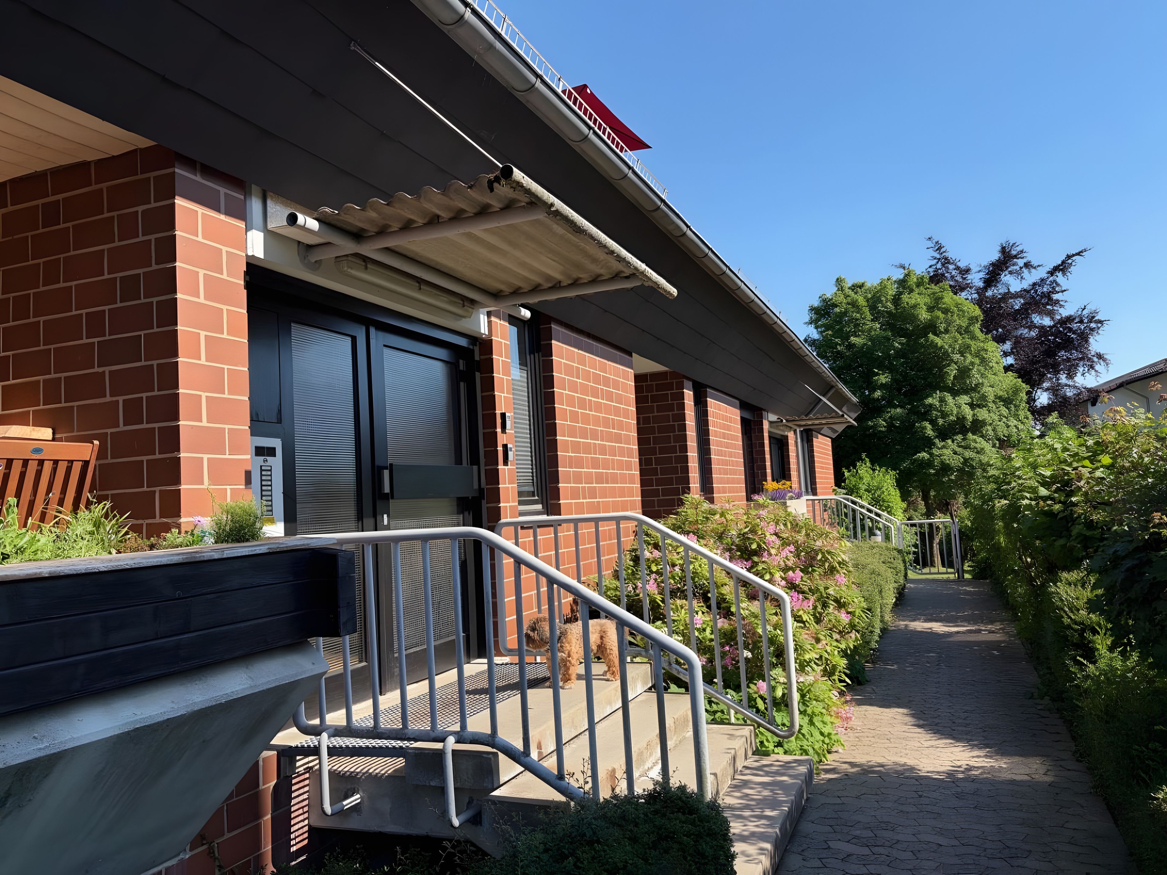 A building with a brick facade, a covered entrance, and a pathway leading to a gated area.