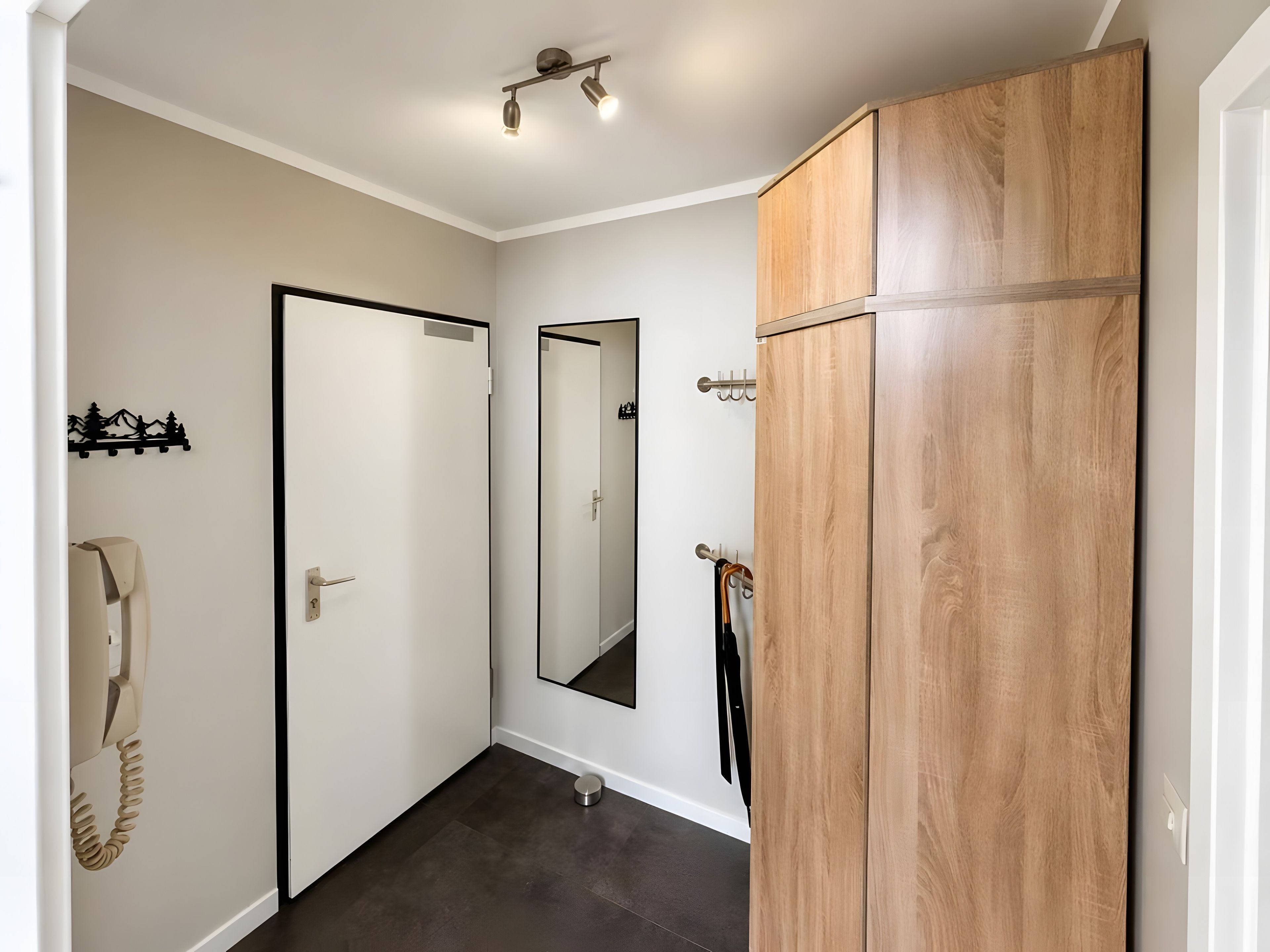 A hallway with a wooden wardrobe, a coat rack, a mirror, and a telephone.