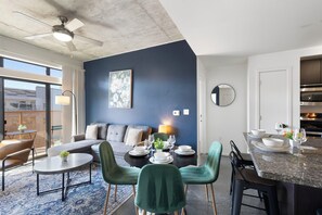 A modern living room with a sofa, dining table, and chairs, a kitchen with a countertop and cabinets, and a ceiling fan. - Lovely 2BR | Pool + W/D | Near Arts District (Phoenix)