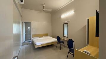 A hotel room with a bed, two chairs, a desk, a mirror, and a ceiling fan.