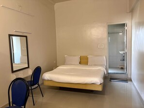 A hotel room with a bed, a chair, a mirror, and a bathroom visible through an open door. - Deluxe Hotel Saubhagyashanti (Nashik)