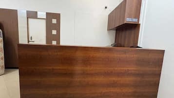 A reception desk with a wooden finish, a white wall, and a door with a check-in/out sign.