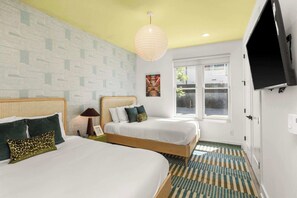 Ein Hotelzimmer mit zwei Betten, einem großen Fenster, einem an der Wand befestigten Fernseher und einem gemusterten Teppich.