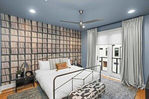 Une chambre à coucher avec un lit, des tables de chevet, un ventilateur de plafond et un mur décoré d’un motif.
