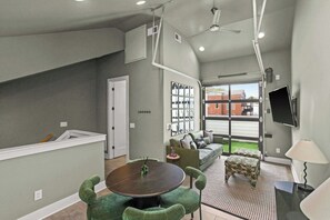 A modern living room with a round table, green upholstered chairs, a sofa, and a television mounted on the wall. - Great Location Near Gulch, 12 South & Broadway (Nashville)