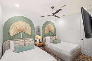 Une chambre d’hôtel avec deux lits, un ventilateur de plafond, une télévision et un miroir.
