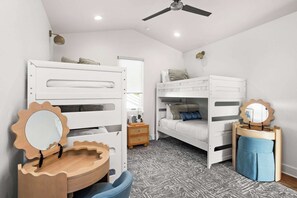 Ein Kinderzimmer mit Etagenbetten, einem hölzernen Schminktisch mit Spiegel und einem Deckenventilator.