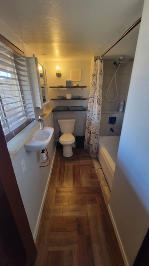 A compact bathroom with a toilet, sink, shower, and a window with blinds. - Perfect View 1-bedroom room with AC in delightful Grand Coulee (Grand Coulee)