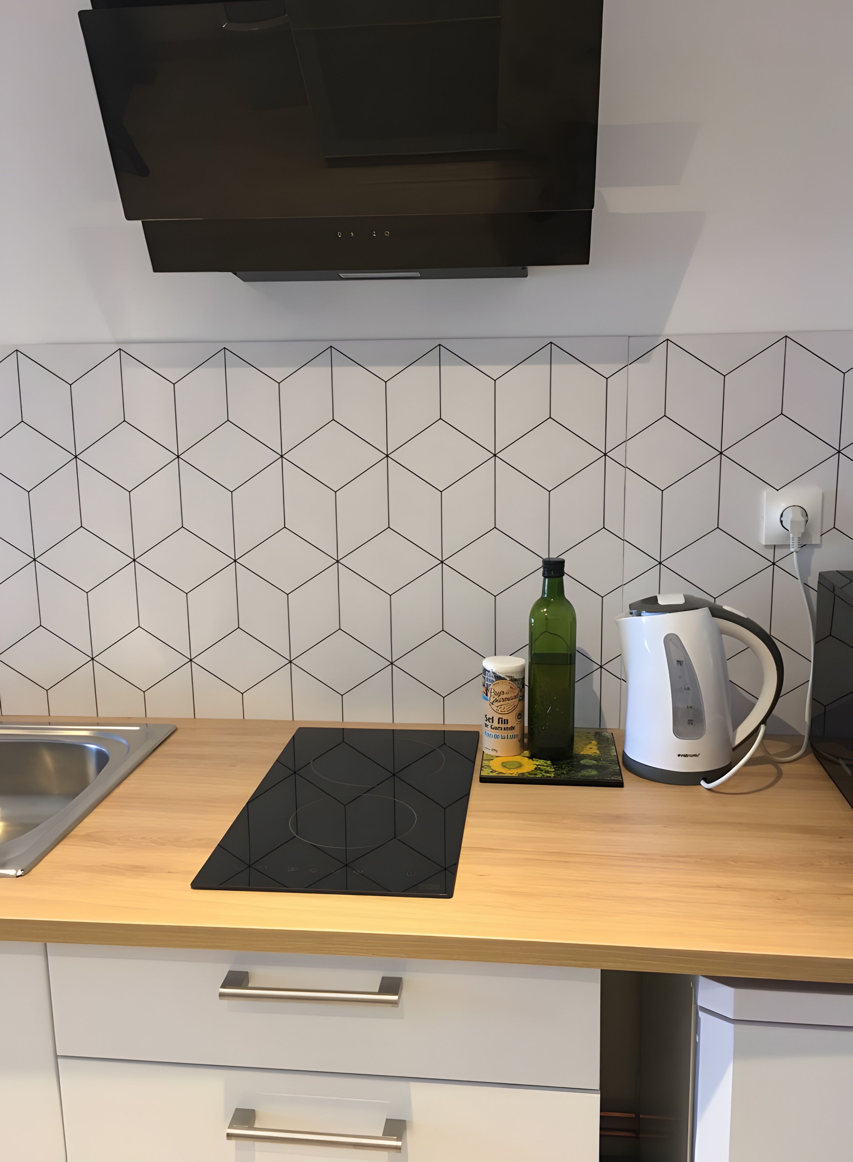 A kitchen with a black induction cooktop, a kettle, and a bottle of olive oil on the counter.