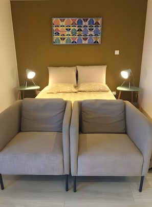 Ein Schlafzimmer mit einem Bett, zwei Nachttischen mit Lampen, einem Sofa und einem geometrischen Kunstwerk an der Wand.