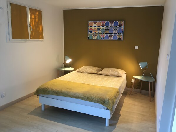 Ein Schlafzimmer mit einem Bett, zwei Nachttischlampen, einem Wandbild und einem Fenster mit Jalousien.