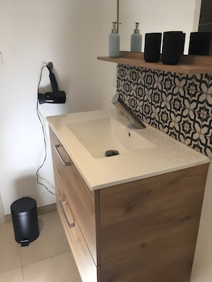 Ein Badezimmer mit einem weißen Waschbecken, einem Holzschrank und einer gemusterten Spritzschutzwand.