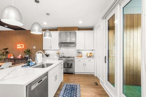 A modern kitchen with white cabinets, a stainless steel stove, and pendant lighting. - Sleeps 24 | Sauna, Peloton, Balcony + Fire pit (Nashville)