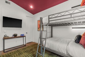 Ein Stockbett mit einer Halterung, ein an der Wand befestigter Fernseher und ein kleiner Tisch mit Büchern und einer Fernbedienung.