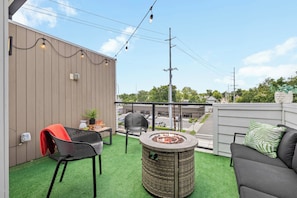 A balcony with artificial grass, a round table with a fire pit, a black chair, and a sofa with a green pillow. - Sleeps 24 | Sauna, Peloton, Balcony + Fire pit (Nashville)