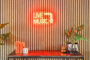 Ein Neon-Schild mit der Aufschrift "LIVE MUSIC" vor einer gestreiften Wand, eine Zimmerpflanze und ein Würfel auf einem Tisch.