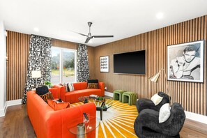 A modern living room with a large flat-screen TV, orange sofas, a coffee table, and a patterned rug. - Sleeps 24 | Sauna, Peloton, Balcony + Fire pit (Nashville)