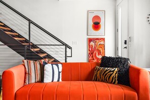 Un saló modern amb un sofà taronja, una escala i art abstracte a les parets.