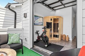 Interior modern d'una casa amb zona de gimnàstic, un sofà amb coixí de motius de fulles verdes i un armari de fusta.