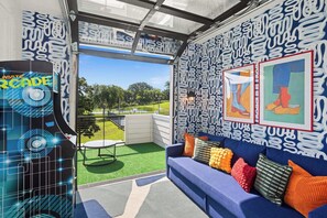 Ein Zimmer mit einem blauen Sofa, bunten Kissen, einer Wand mit Muster und Blick auf einen Park.