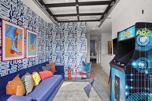 A modern living room with a blue sofa, colorful cushions, a red chair, and a retro arcade machine. - 8 Beds | Minutes to Broadway, Gulch & 12 South (Nashville)
