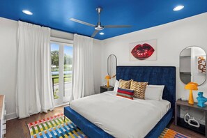 Een slaapkamer met een groot bed, een plafondventilator, een raam met gordijnen, lippenstiftkunst en een spiegel.