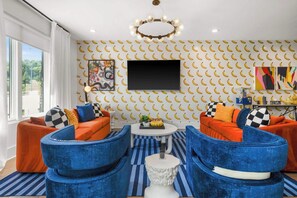 Ein modernes Wohnzimmer mit orangefarbenen Sofas, blauen Sesseln, einem Flachbildfernseher und einer Wand mit Muster.