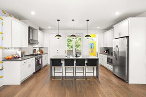A modern kitchen with white cabinets, a central island with bar stools, stainless steel appliances, and wooden flooring. - 8 Beds | Minutes to Broadway, Gulch & 12 South (Nashville)