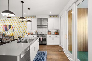 A modern kitchen with white cabinets, a stainless steel sink, and a large island. There are pendant lights, a tiled backsplash, and a wooden floor. - 8 Beds | Minutes to Broadway, Gulch & 12 South (Nashville)