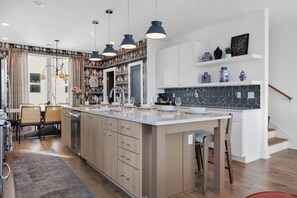 Uma cozinha moderna com ilha central, luminárias pendentes e uma área de refeições com cadeiras e mesa.