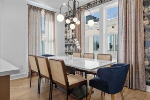 Ein Essbereich mit einem Marmortisch, Korbstühlen und gepolsterten Sesseln, einer Kristallleuchter und Blick auf einen Balkon.