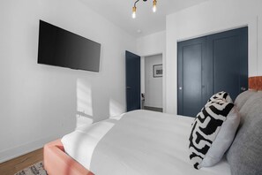 A bedroom with a bed, a flat-screen TV mounted on the wall, a dark door, and a light switch. - Hot Tub Hang Grill Parking  Views of Downtown (Nashville)