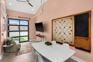 A room with a large window, a white table, a television, and a Scrabble board. - 8 Beds | Minutes to Broadway, Gulch & 12 South (Nashville)
