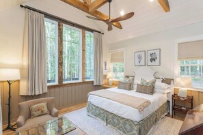 A bedroom with a large bed, two windows with curtains, a ceiling fan, and a nightstand with a lamp. - 7  Cottages at Buckhorn Hollow - Sleeps 28 (McEwen)