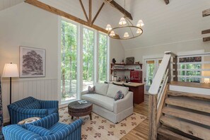 A cozy living room with a sofa, two armchairs, a coffee table, and a staircase. - 7  Cottages at Buckhorn Hollow - Sleeps 28 (McEwen)