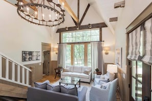 A spacious living room with a high ceiling, a staircase, and large windows offering a view of the outdoors. - 7  Cottages at Buckhorn Hollow - Sleeps 28 (McEwen)