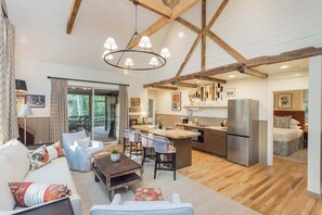 A spacious living area with a large sofa, a coffee table, and a kitchen area with a refrigerator, sink, and bar stools. - 7  Cottages at Buckhorn Hollow - Sleeps 28 (McEwen)