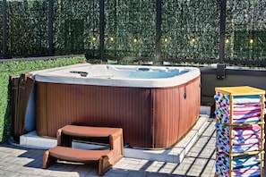Uma banheira de hidromassagem com exterior em madeira, um banco de madeira e uma pilha de toalhas coloridas.