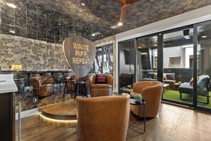 A modern lounge area with leather sofas, a wooden accent wall, and a large window offering a view of the outdoors. - Songwriters' Retreat: 4BR, Rooftop Sauna & Bar (Nashville)