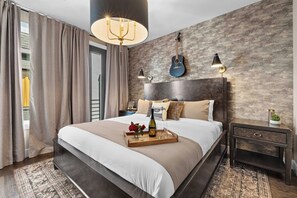A modern bedroom with a large bed, a chandelier, a guitar, and a nightstand. - Songwriters' Retreat: 4BR, Rooftop Sauna & Bar (Nashville)