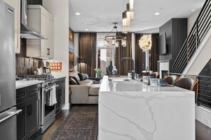 A modern kitchen with stainless steel appliances, a marble island, and a dining area with leather chairs. - Songwriters' Retreat: 4BR, Rooftop Sauna & Bar (Nashville)